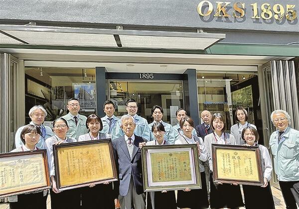 神戸本社社員と奥谷社長(右)、奥谷会長(前列左から4人目)。賞状は右から、「神戸貿易品品評会」褒状、内国勧業博覧会の褒状、神戸市製産物品評会の有功賞